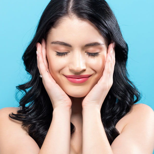 woman with her eyes closed, touching her face, and smiling